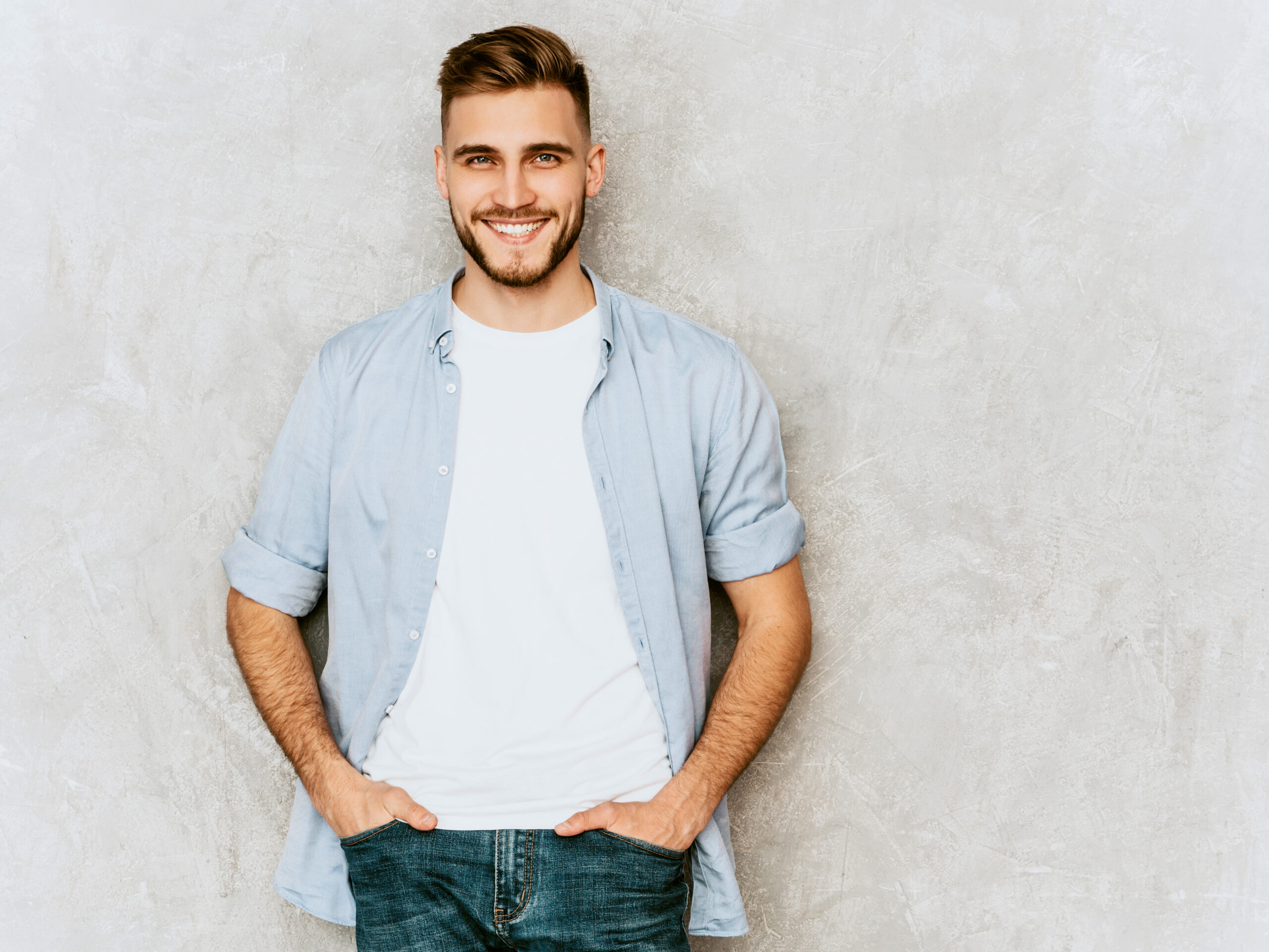 Portrait of handsome smiling hipster lumbersexual businessman model wearing casual shirt clothes. Fashion stylish man posing against gray wall